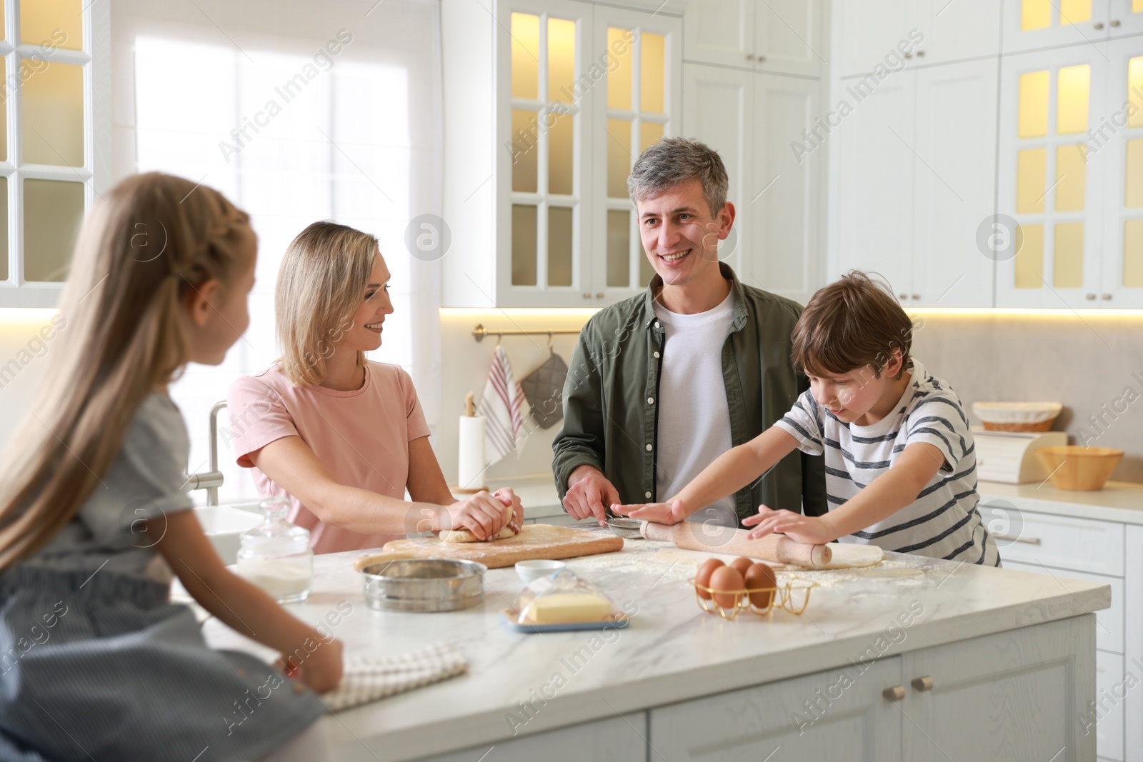 Photo of Happy family kneading dough at white marble table in kitchen