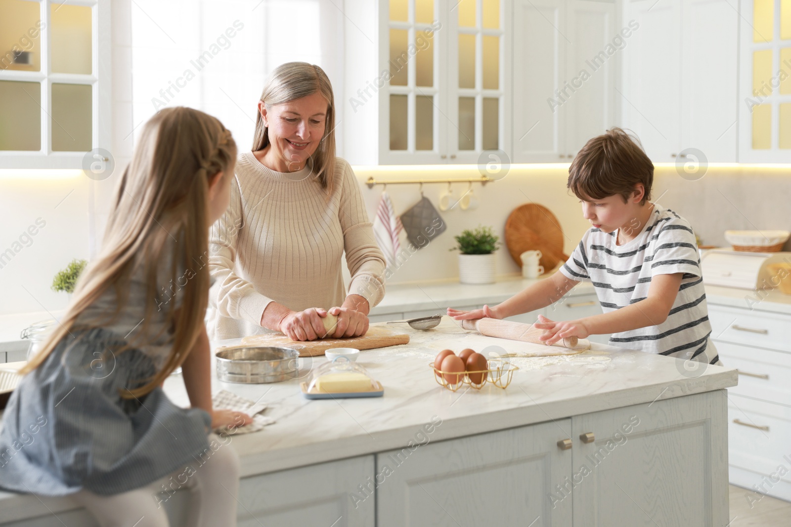 Photo of Grandmother and her grandchildren making dough at white marble table in kitchen