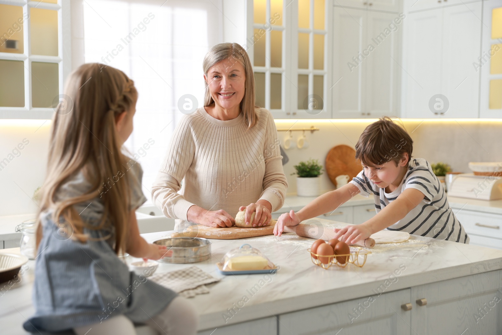 Photo of Grandmother and her grandchildren making dough at white marble table in kitchen