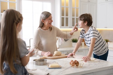 Photo of Grandmother and her grandchildren making dough at white marble table in kitchen