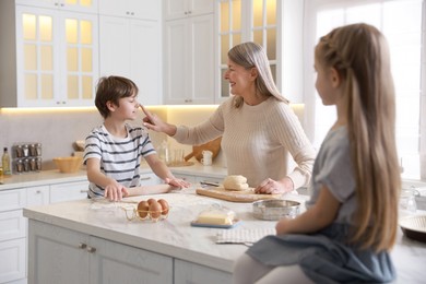 Photo of Grandmother and her grandchildren making dough at white marble table in kitchen