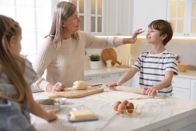 Photo of Grandmother and her grandchildren making dough at white marble table in kitchen