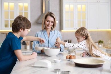 Photo of Mother and her kids making dough at white marble table in kitchen