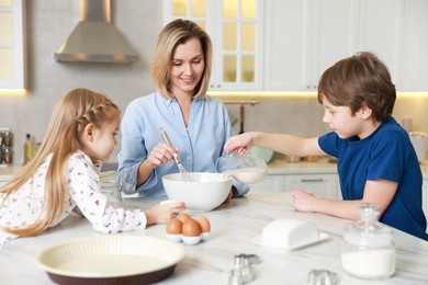 Photo of Mother and her kids making dough at white marble table in kitchen