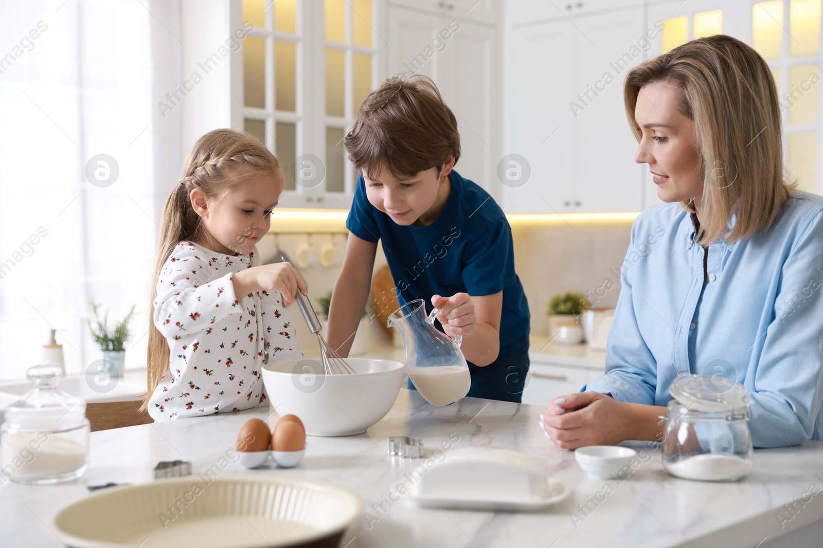 Photo of Mother and her kids making dough at white marble table in kitchen