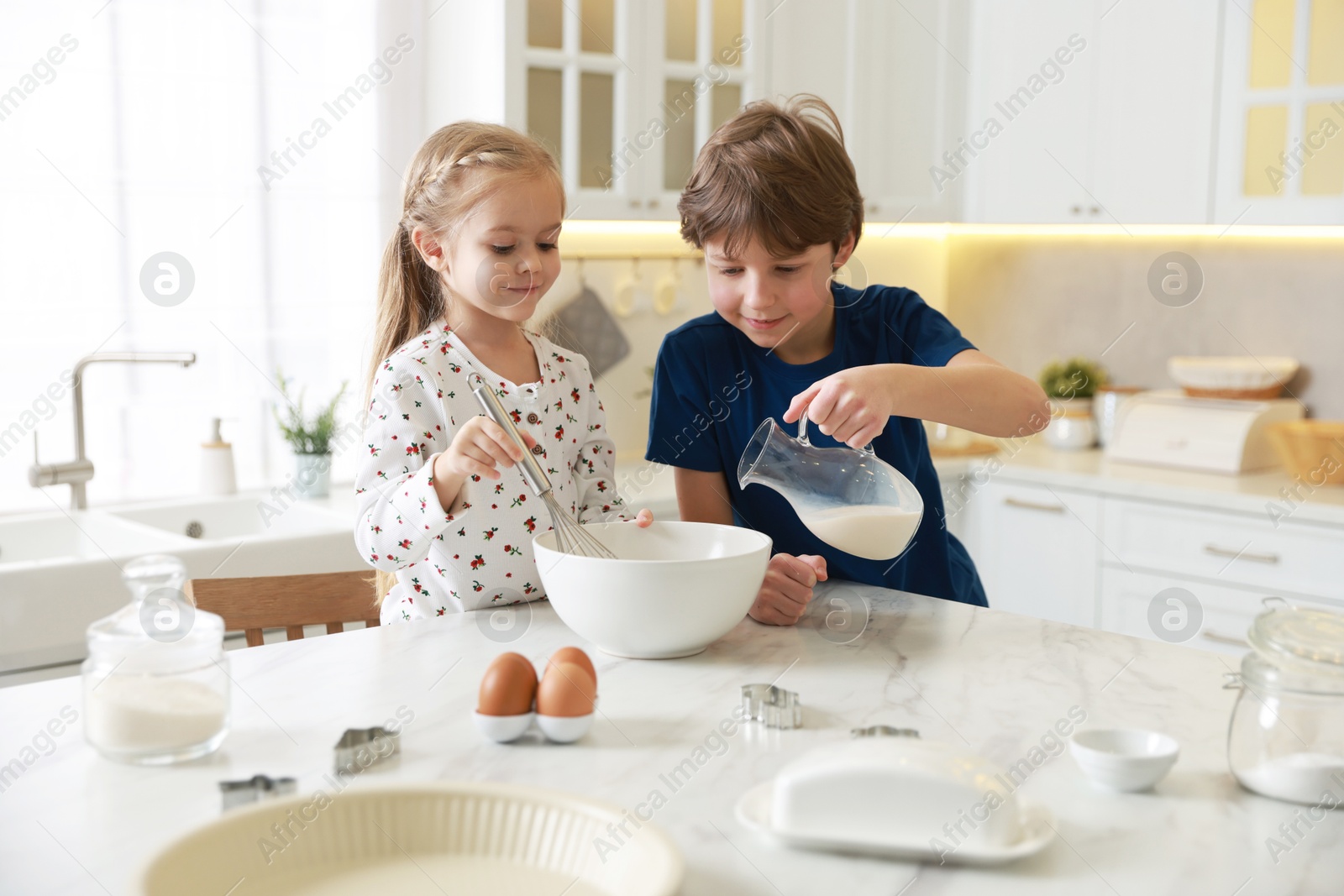 Photo of Little kids making dough at white marble table in kitchen