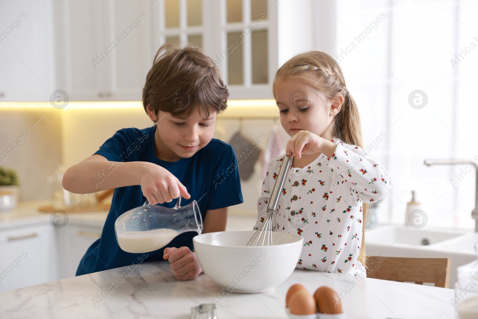 Photo of Little kids making dough at white marble table in kitchen