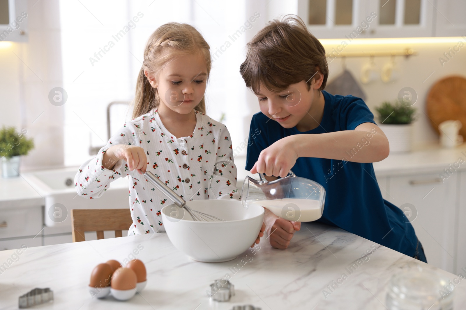 Photo of Little kids making dough at white marble table in kitchen