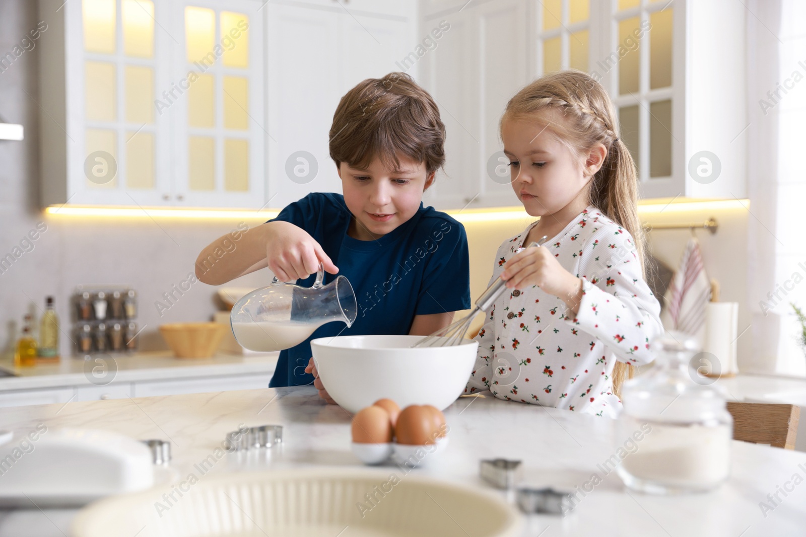 Photo of Little kids making dough at white marble table in kitchen