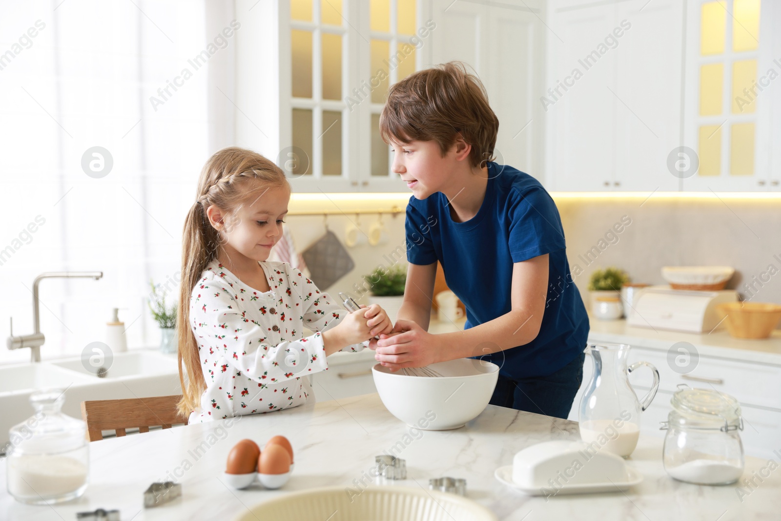 Photo of Little kids making dough at white marble table in kitchen