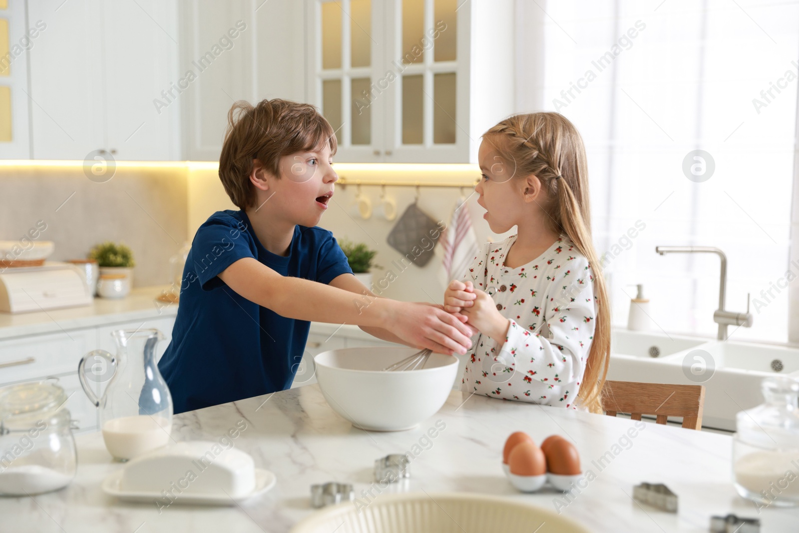 Photo of Little kids making dough at white marble table in kitchen