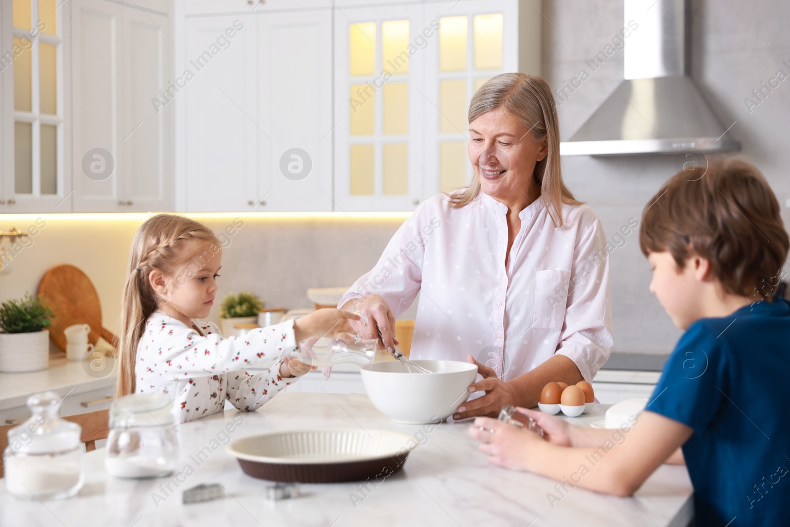 Photo of Grandmother and her grandchildren making dough at white marble table in kitchen