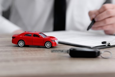 Photo of Man signing purchase agreement at wooden table, focus on car model. Buying auto