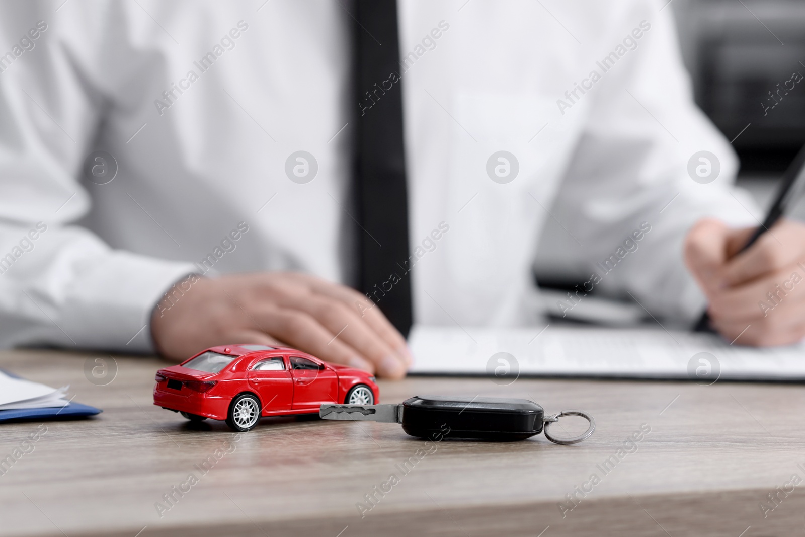 Photo of Man signing purchase agreement at wooden table, focus on key and car model. Buying auto