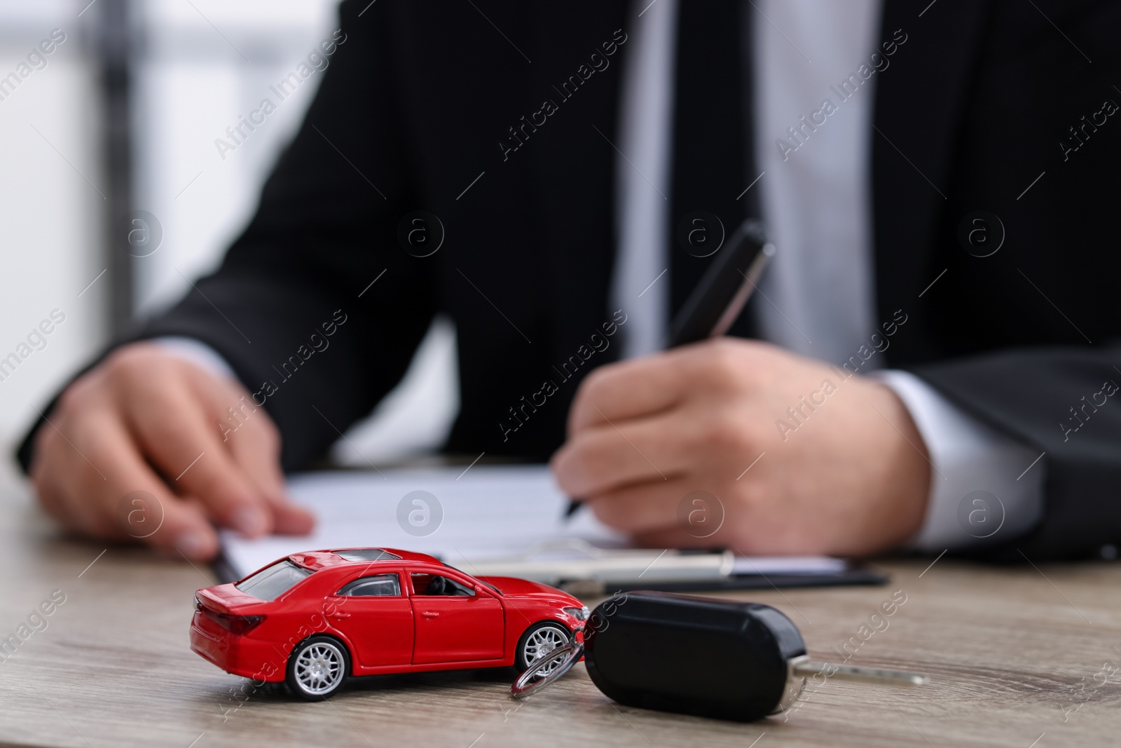 Photo of Man signing purchase agreement at wooden table, focus on car model and key. Buying auto