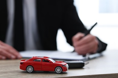 Photo of Man signing purchase agreement at wooden table, focus on car model. Buying auto