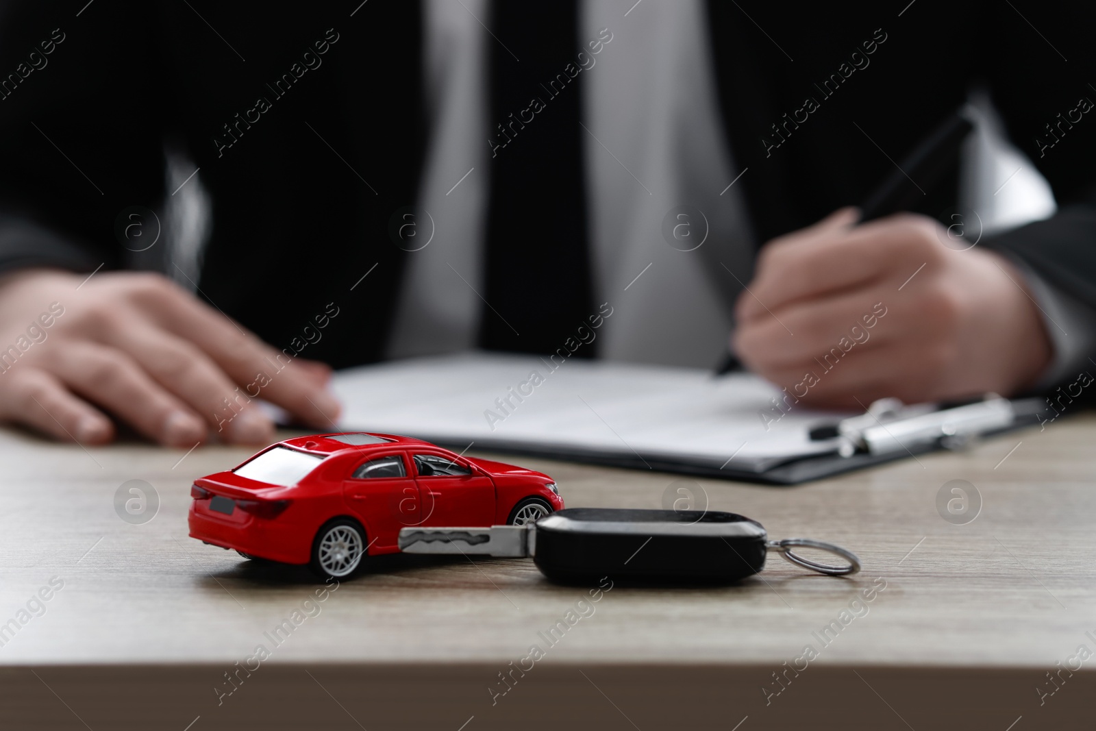 Photo of Man signing purchase agreement at wooden table, focus on car model and key. Buying auto