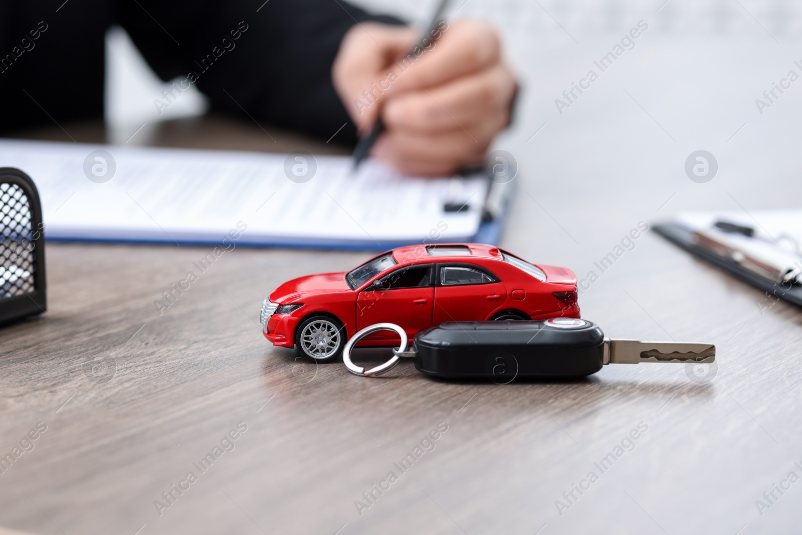 Photo of Man signing purchase agreement at wooden table, focus on car model and key. Buying auto