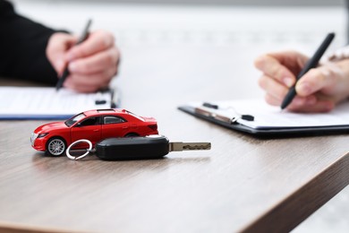 Photo of Salesman and client signing documents at wooden table, focus on car model and key. Buying auto