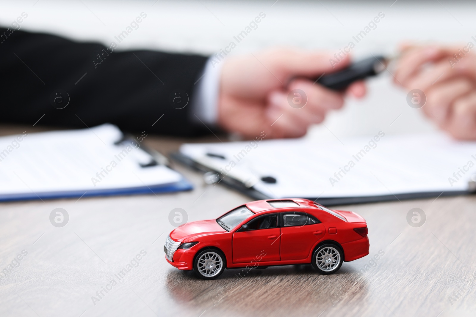 Photo of Salesman giving key to buyer at wooden table in office, focus on car model. Buying auto