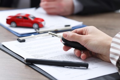 Photo of Salesman with key and documents at wooden table in office, closeup. Buying auto