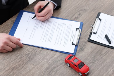 Photo of Man signing car purchase agreement at wooden table, closeup. Buying auto