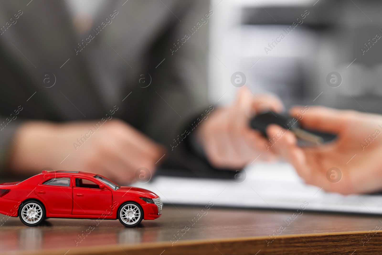 Photo of Buying auto. Client getting key at wooden table, focus on red car model