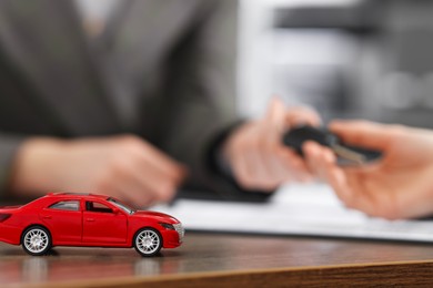 Photo of Buying auto. Client getting key at wooden table, focus on red car model