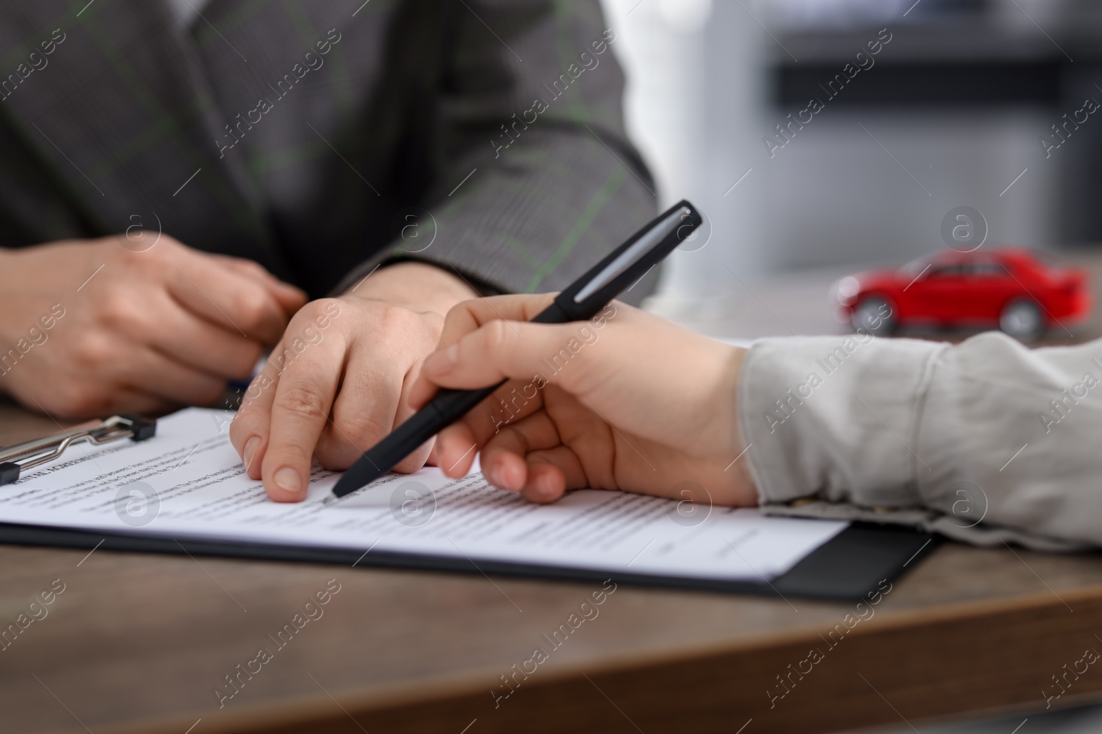 Photo of Manager and client signing car purchase agreement at wooden table, selective focus. Buying auto