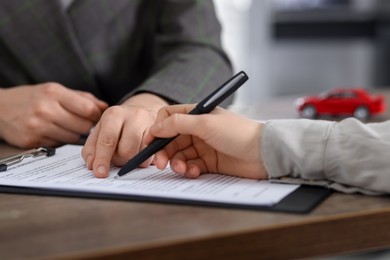 Photo of Manager and client signing car purchase agreement at wooden table, selective focus. Buying auto