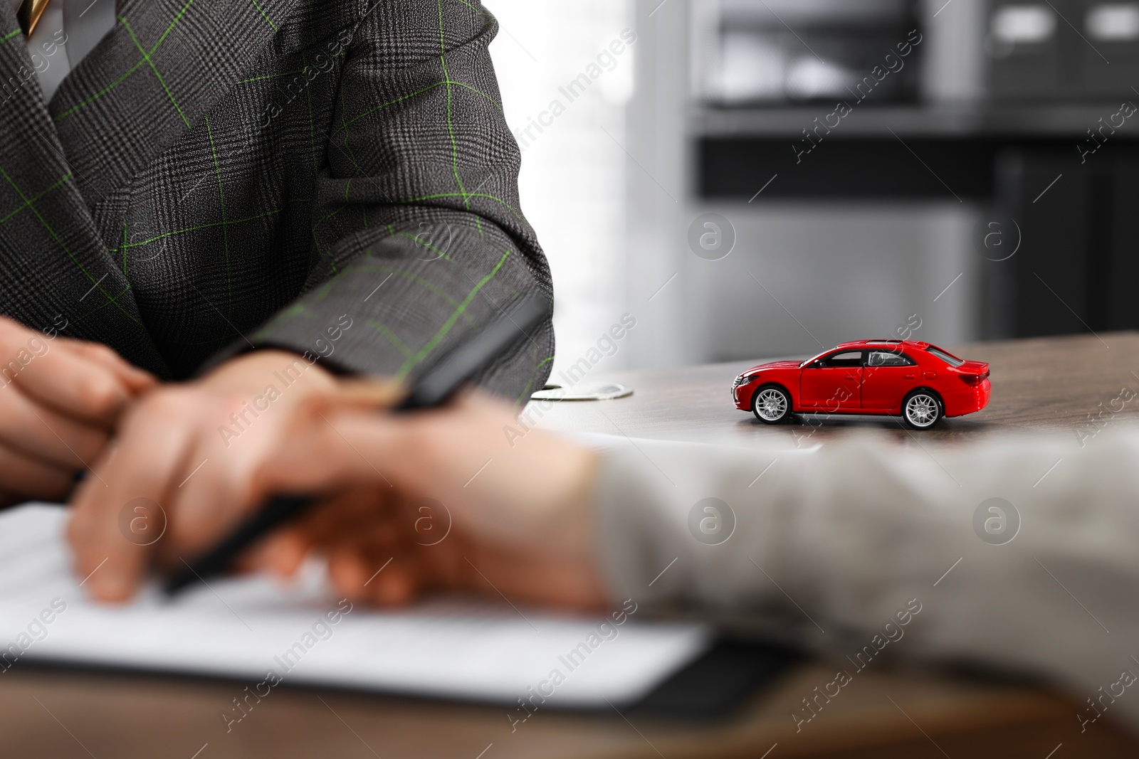 Photo of Manager and client signing car purchase agreement at wooden table, selective focus. Buying auto