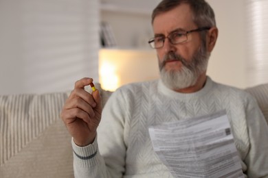 Photo of Senior man with pill and instruction indoors, selective focus