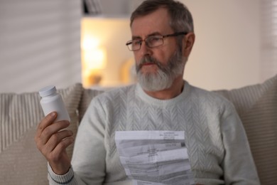 Photo of Senior man with bottle of pills and instruction at home, selective focus