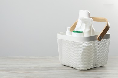 Photo of Different cleaning products in basket on wooden table, space for text