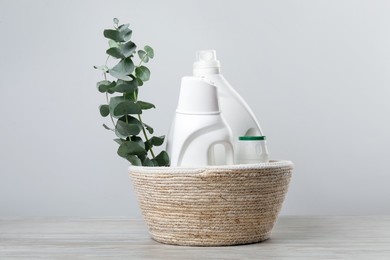 Photo of Eco-friendly cleaning products and eucalyptus branches in wicker basket on wooden table