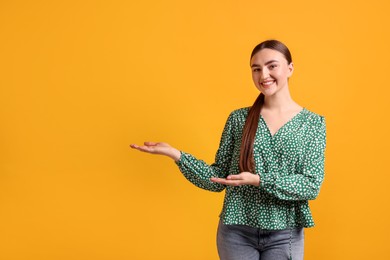 Photo of Cheerful woman welcoming guests on orange background. Space for text