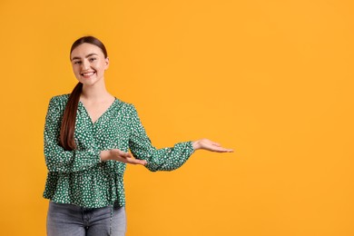 Photo of Cheerful woman welcoming guests on orange background. Space for text