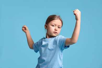 Photo of Cute little girl showing her biceps on light blue background