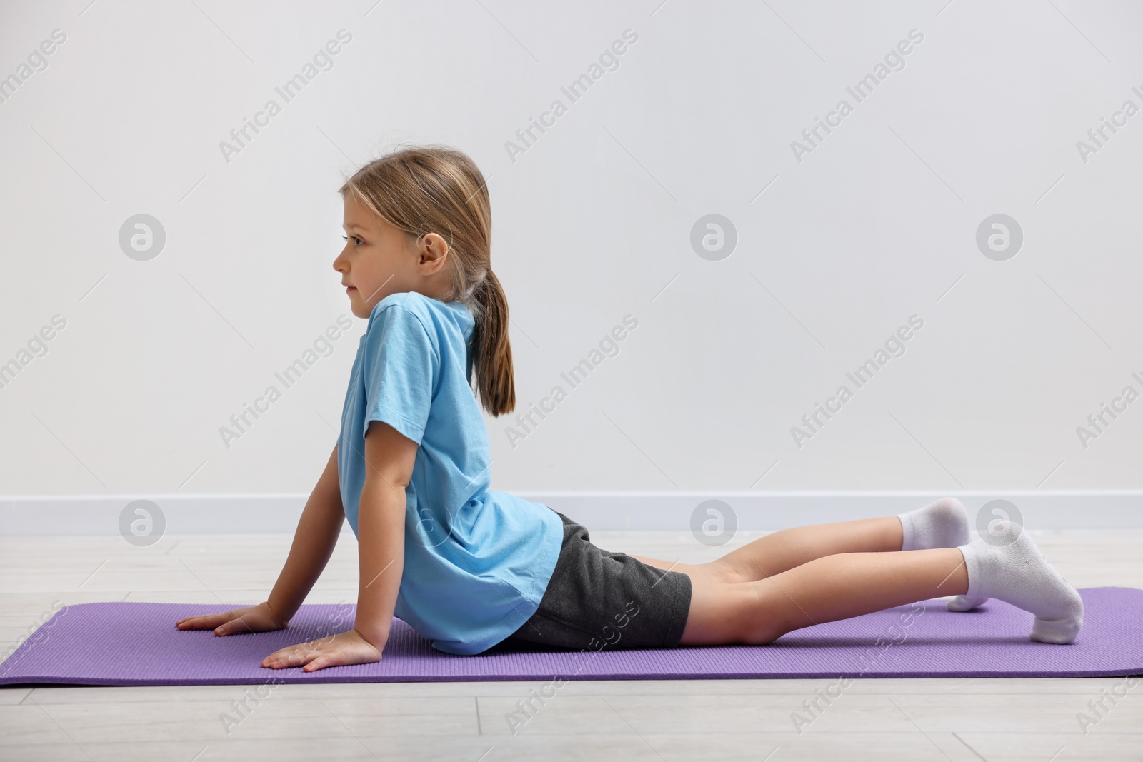 Photo of Cute little girl exercising on fitness mat indoors