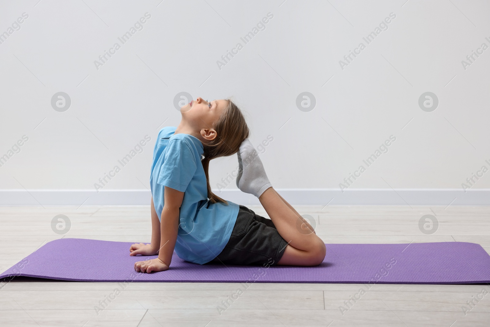 Photo of Cute little girl exercising on fitness mat indoors