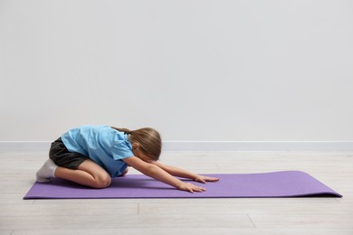 Photo of Cute little girl exercising on fitness mat indoors, space for text