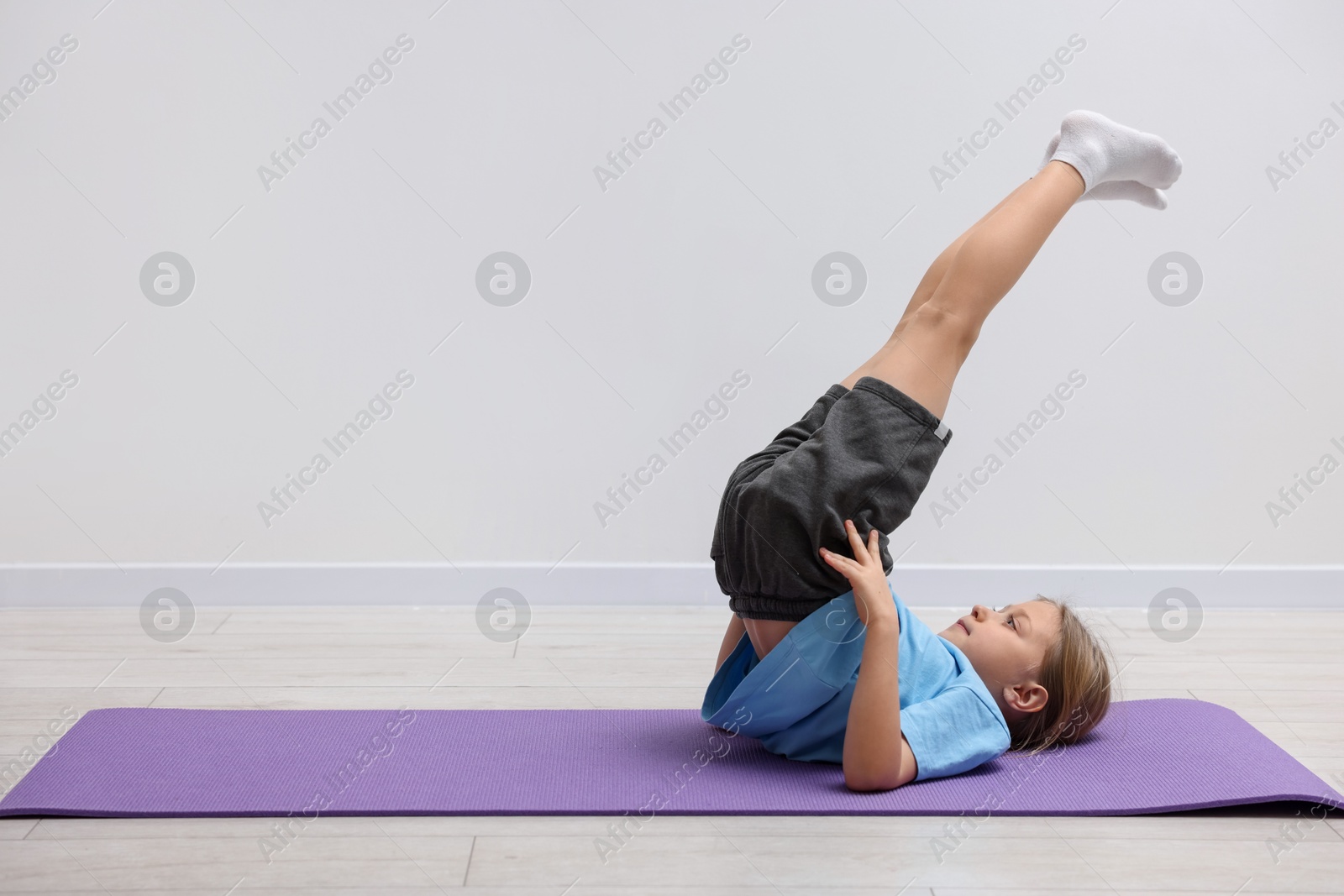 Photo of Cute little girl exercising on fitness mat indoors, space for text