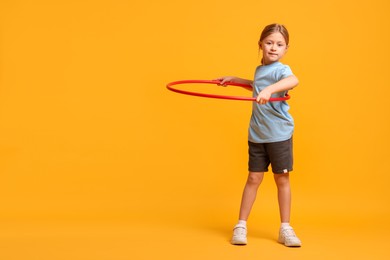 Photo of Cute little girl exercising with hula hoop on orange background, space for text