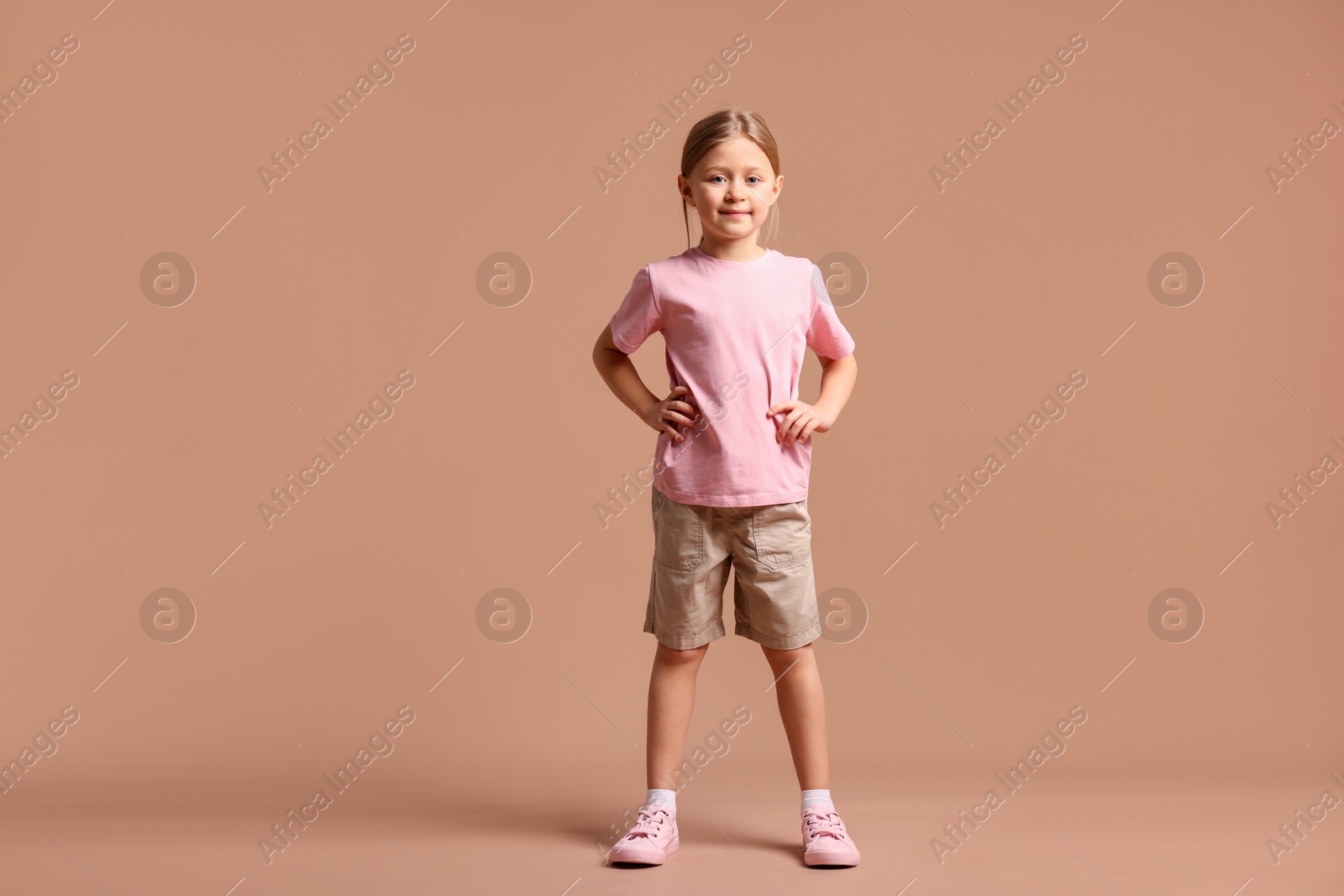 Photo of Cute little girl in sportswear on dark beige background