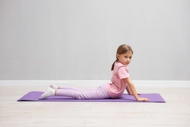 Photo of Cute little girl exercising on fitness mat near grey wall indoors