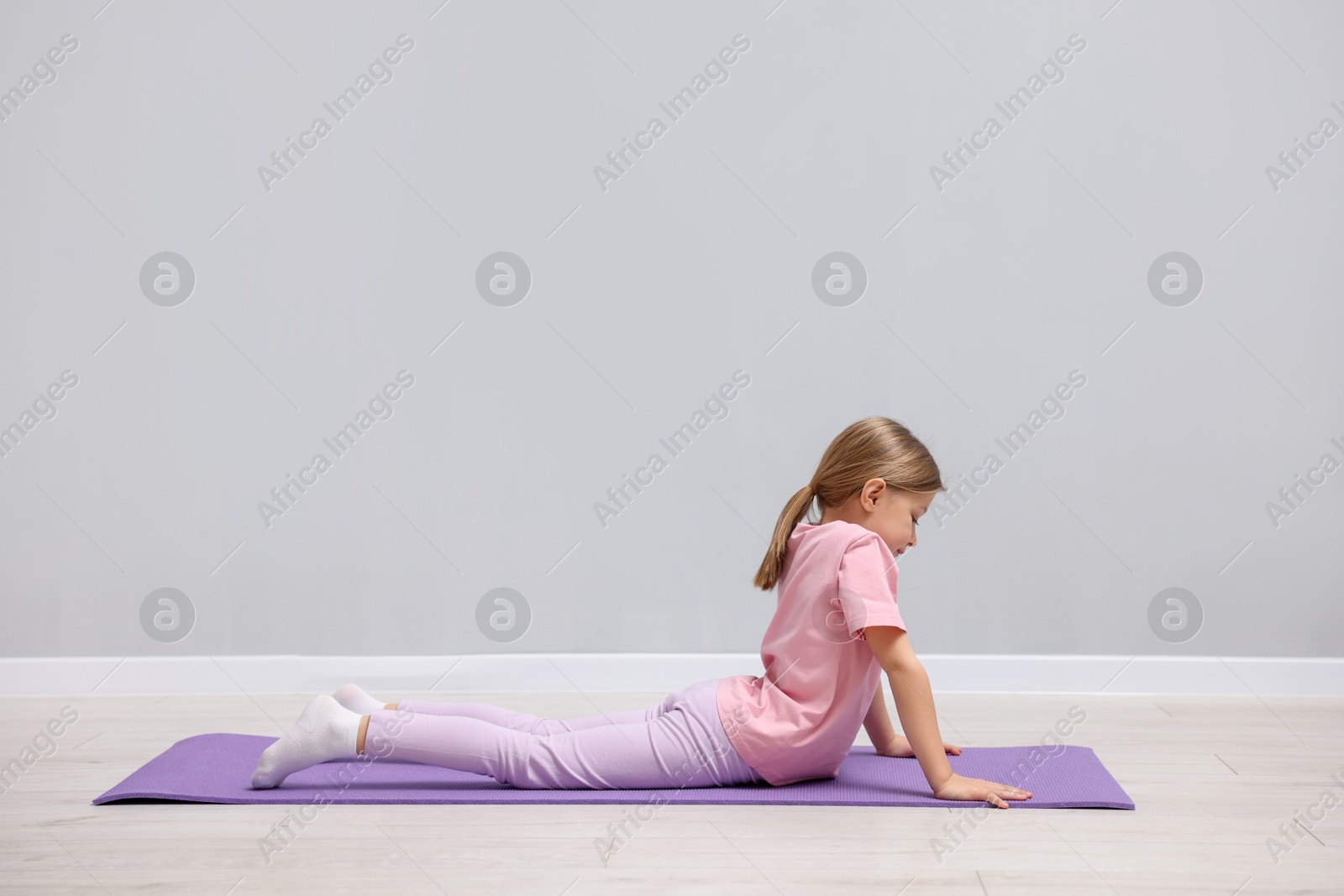 Photo of Cute little girl exercising on fitness mat near grey wall indoors