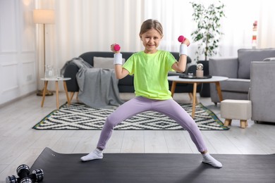 Photo of Cute little girl exercising with dumbbells indoors