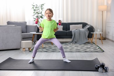 Photo of Cute little girl exercising with dumbbells indoors