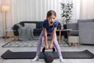 Photo of Cute little girl exercising with kettlebell indoors