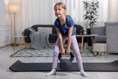 Photo of Cute little girl exercising with kettlebell indoors